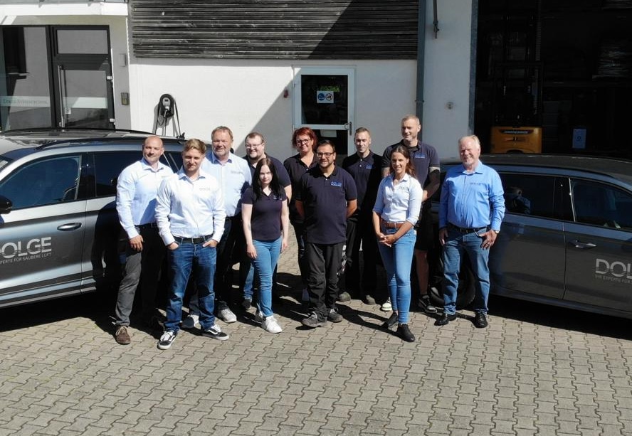 11 Mitarbeiter auf einem Gruppenbild mit zwei Autos draußen